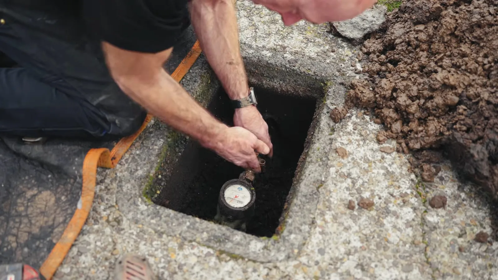 Man reaching an arm down into an in-ground water meter box