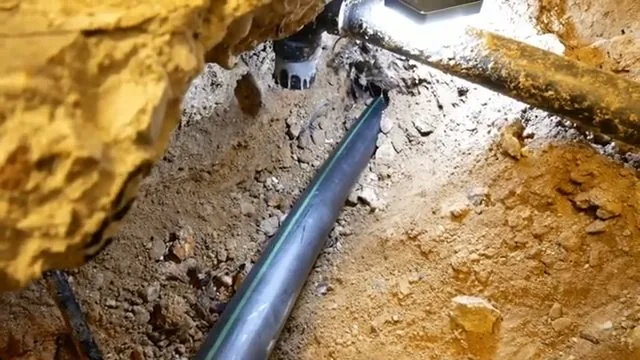 Black pipe lying in an excavated trench with a cleanout fitting at the top