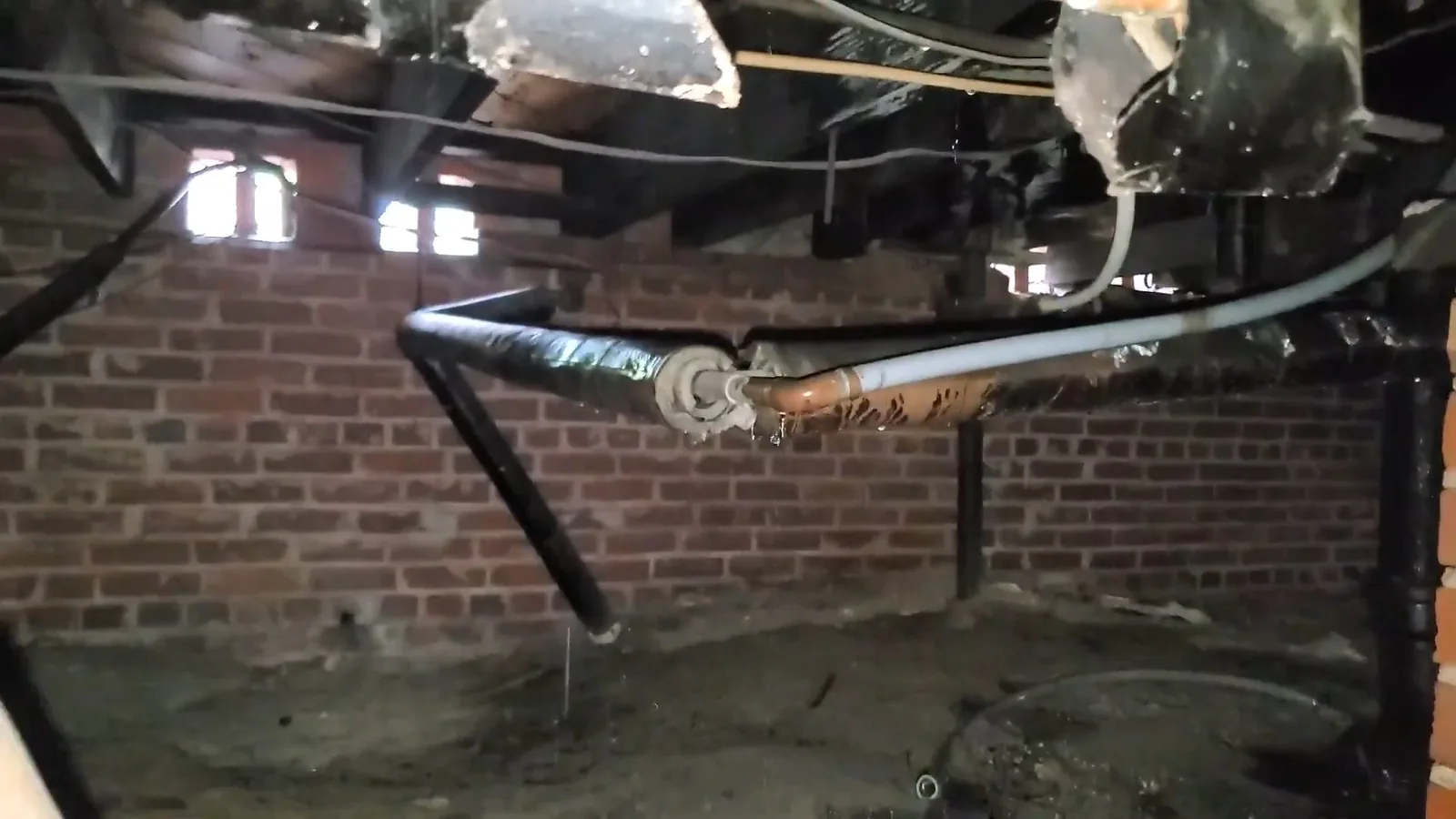 Brick foundation wall in a crawlspace with a black pipe and a copper water line running along it