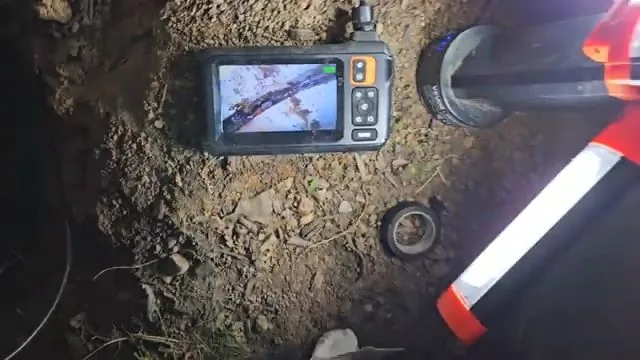 Inspection monitor lying on dirt beside a pipe opening with a work light