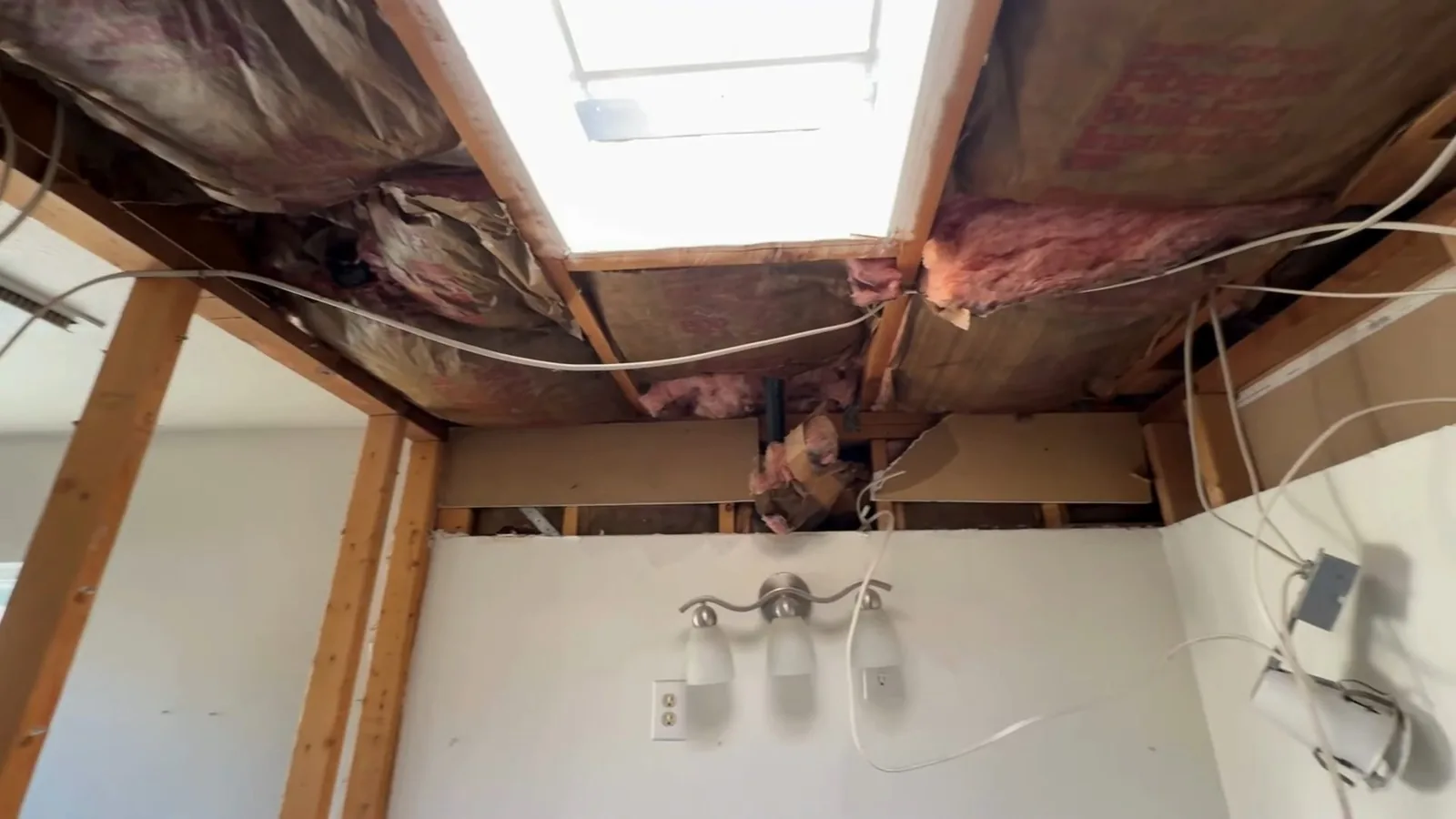 Opened ceiling showing joists and insulation above a bathroom light fixture