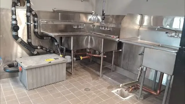 Stainless three-compartment kitchen sink with a grease trap beside black waste piping