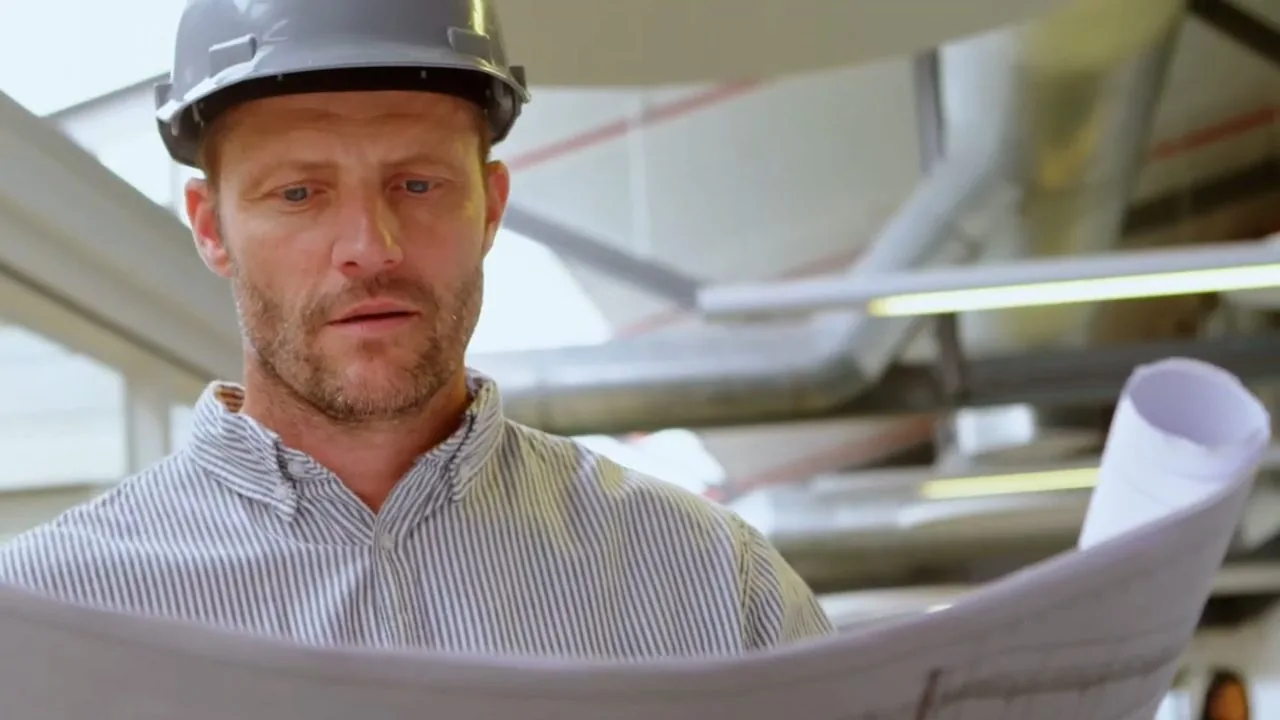 Man in a hard hat reading a set of printed plans