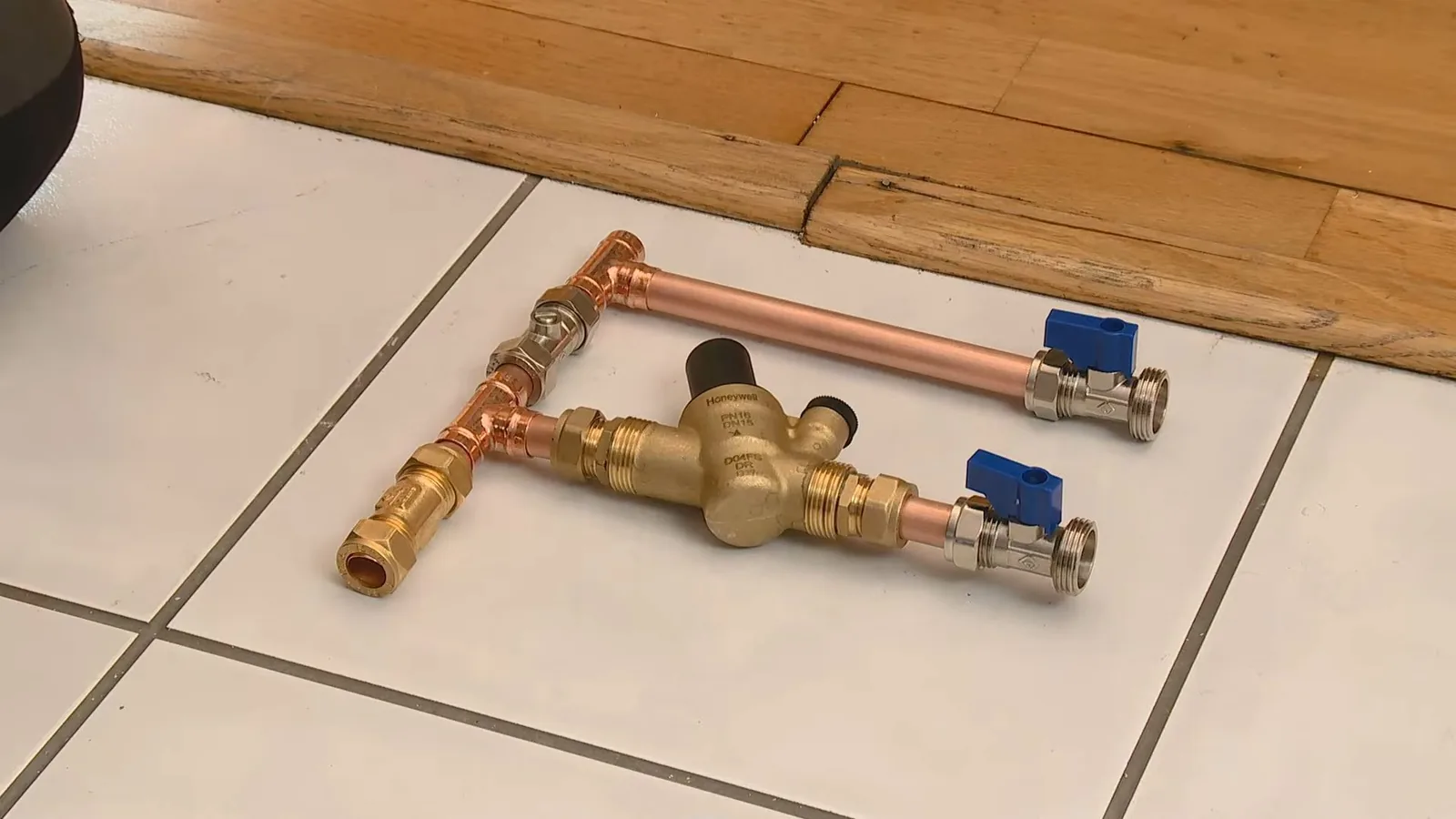 Copper and brass pressure reducing valve with two blue ball valves laid on a tile floor