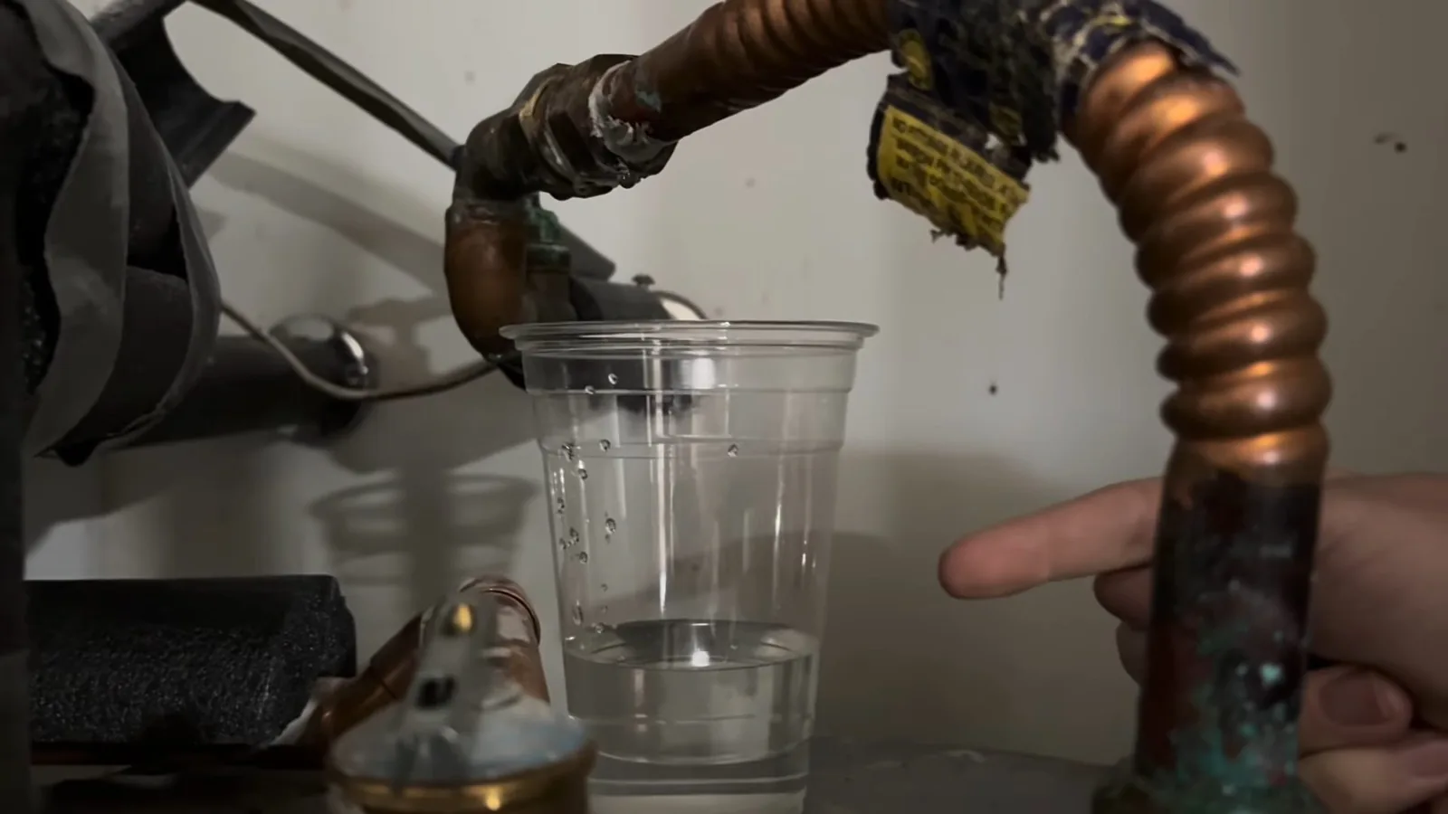Copper and corrugated lines at the top of a water heater with a clear cup of water beneath them