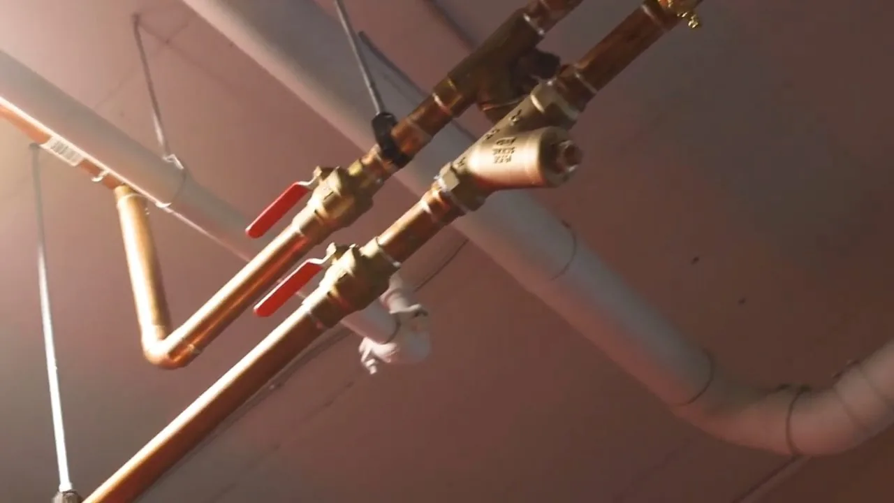 Copper water pipes on a wall with two ball valves that have red handles