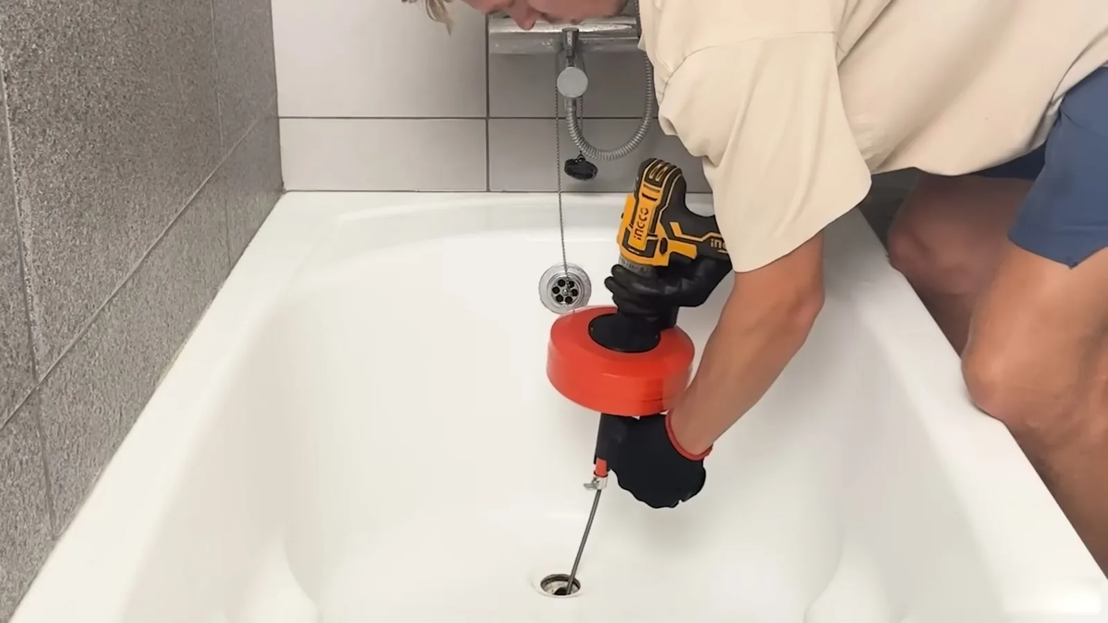 Man feeding a cordless drain auger with an orange drum into a bathtub drain