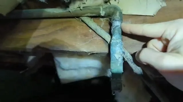 Finger beside a green-corroded copper elbow in a crawlspace