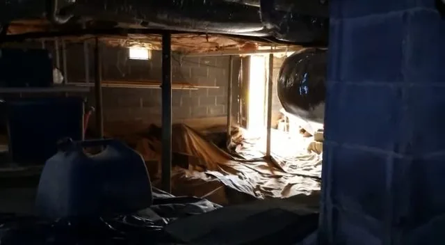 Crawlspace with plastic sheeting on the ground, a post and a supply pipe overhead