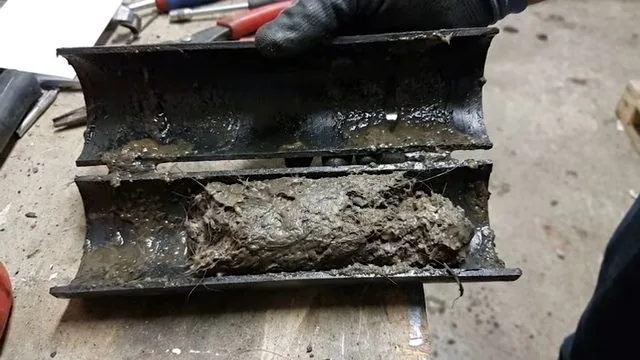 Pipe section cut open lengthwise with thick sludge packed inside
