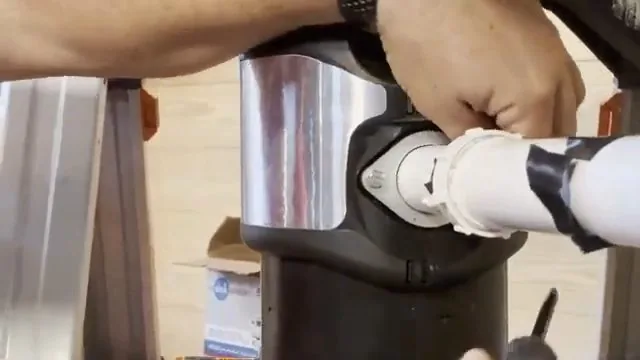 Hands fitting a white discharge pipe to the side port of a garbage disposal on a workbench
