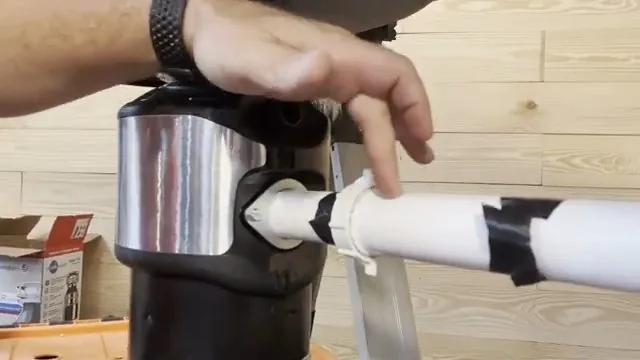 Hand on the white discharge pipe connected to a garbage disposal set on a workbench