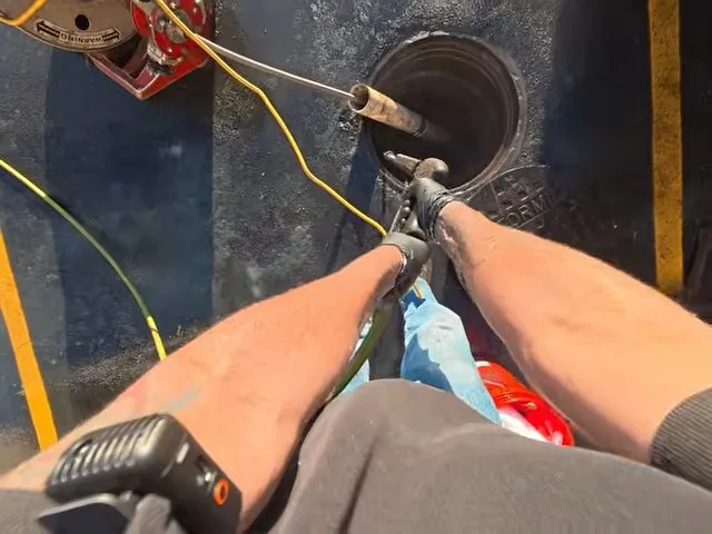 First-person view of a drain machine cable feeding into a round floor drain opening