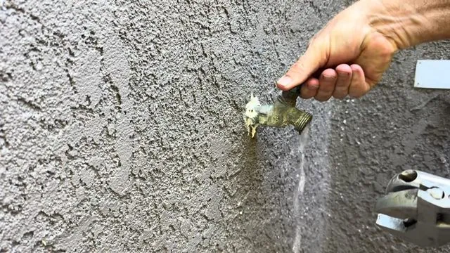Outdoor hose bib on a stucco wall with water running down the wall below the handle