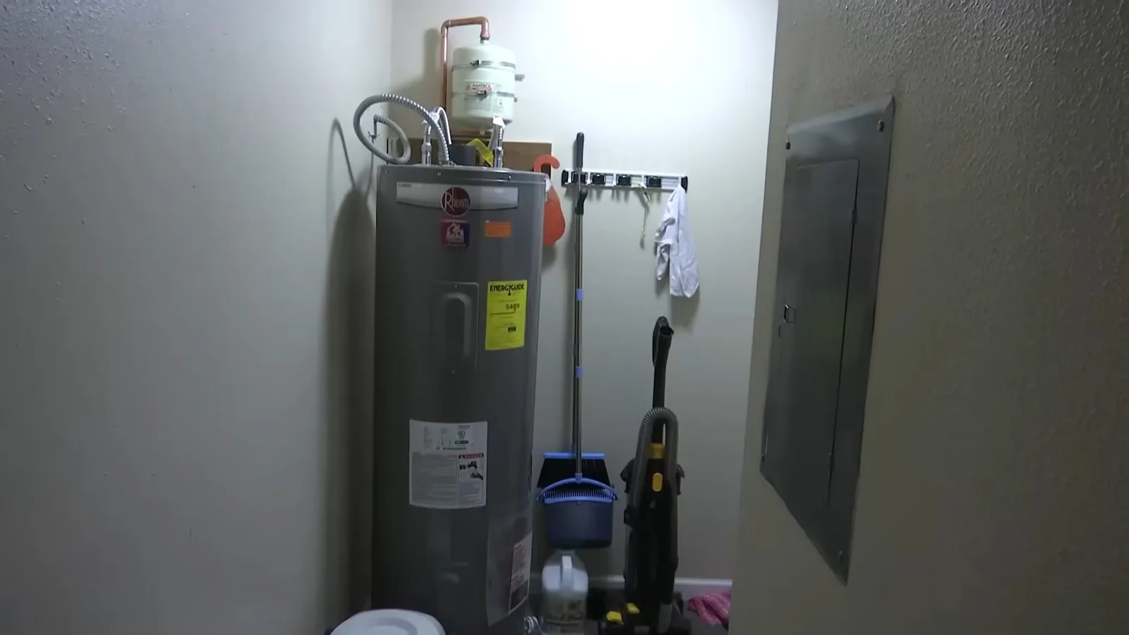Electric tank water heater standing in a narrow utility closet beside a breaker panel