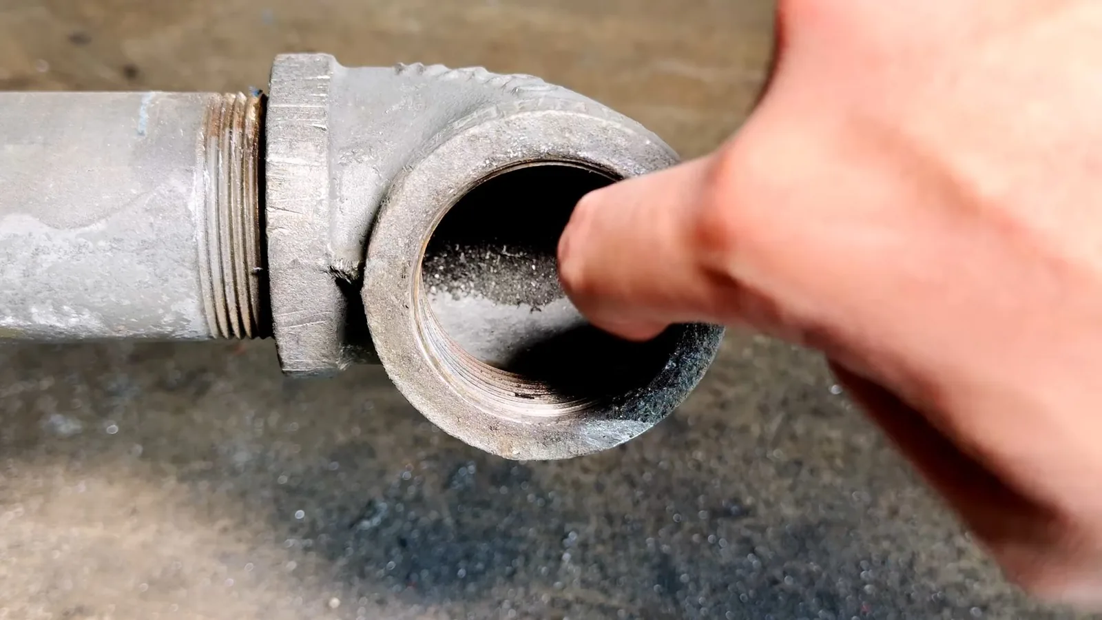 Finger resting at the open threaded end of a galvanized pipe elbow
