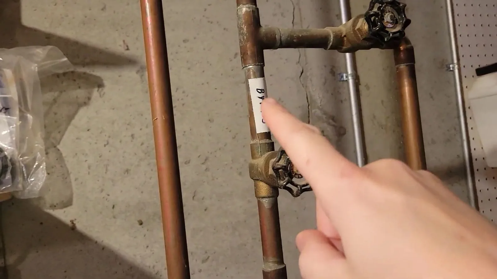 Finger pointing at two copper shutoff valves on a water line beside a wall
