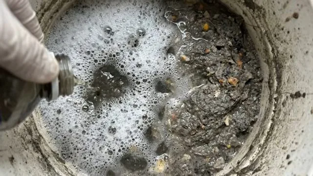 Foamy gray water and debris in a round cleanout pit with a hose entering from the left