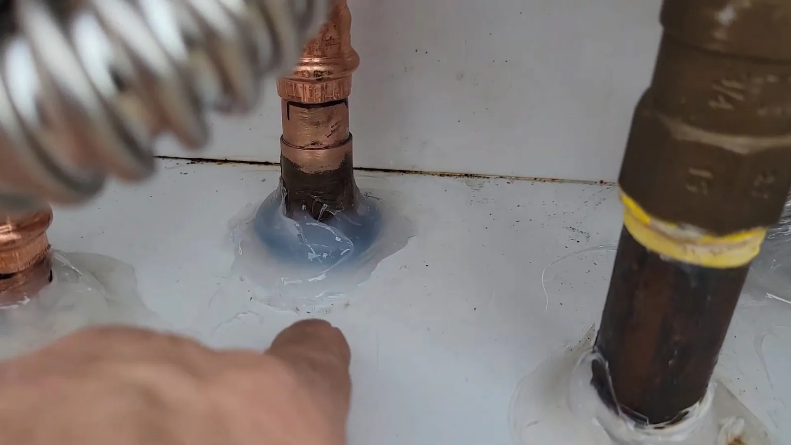 Top of a gas tank water heater with copper and gas connections and blue sealant on a fitting