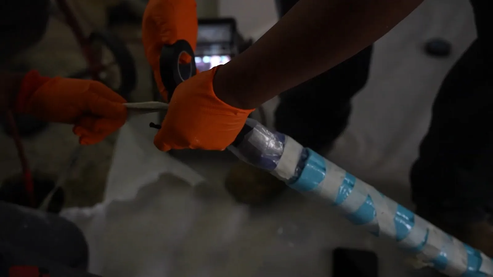 Gloved hands handling a blue-striped section of pipe liner