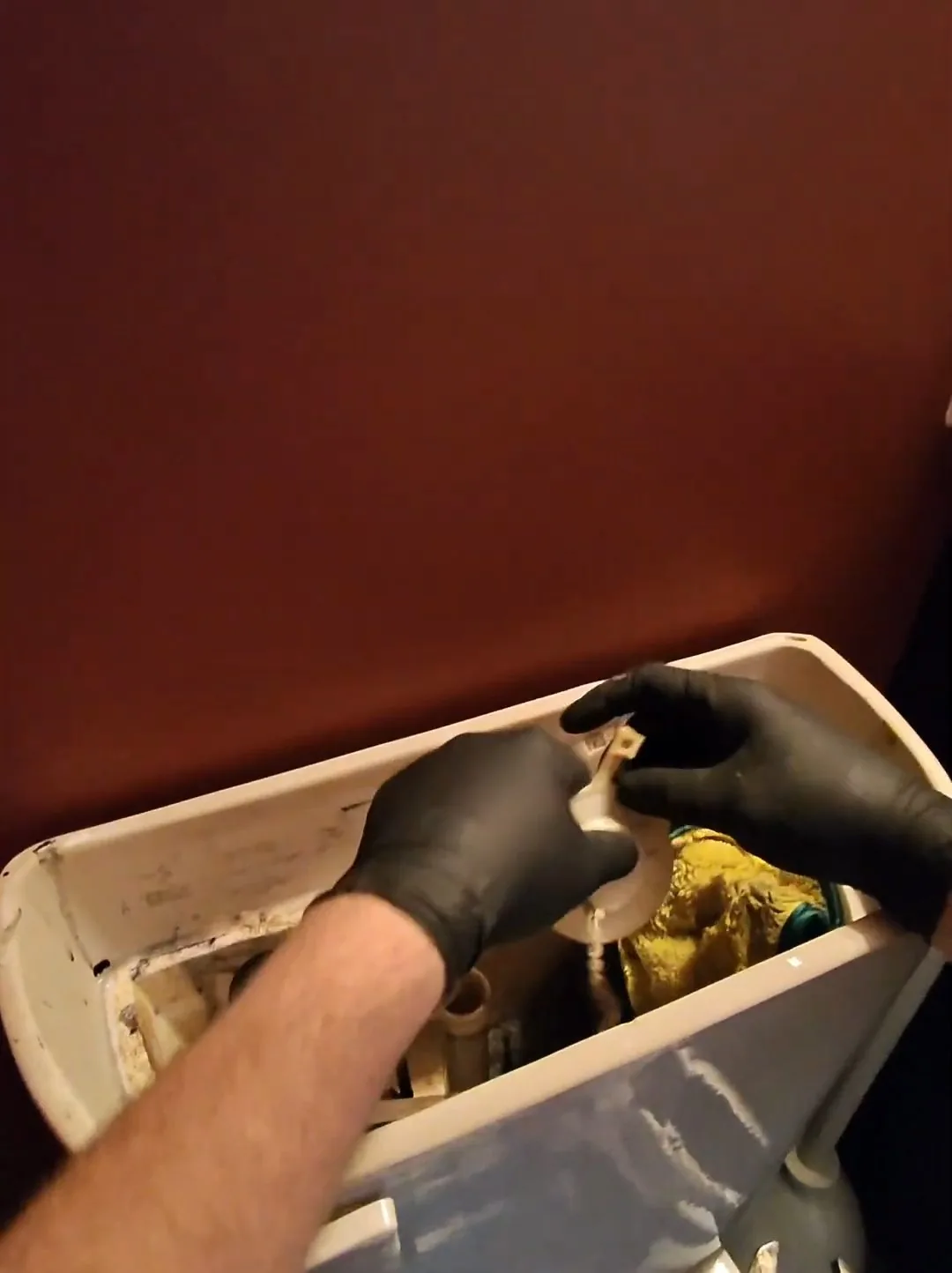 Black-gloved hands working inside the open tank of a toilet