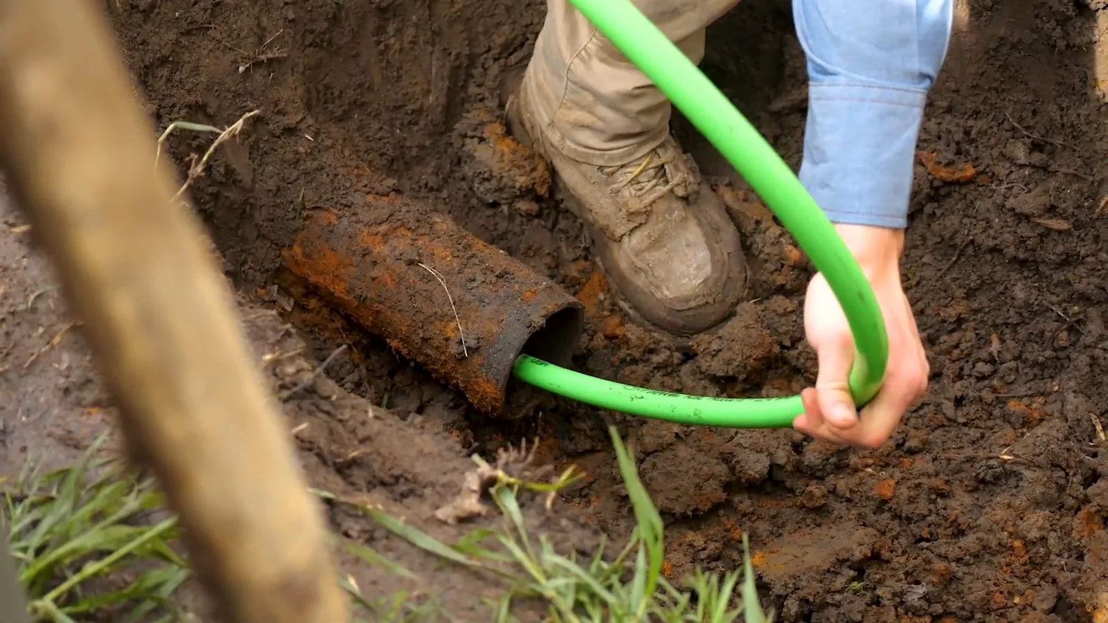 Green liner tube pulled out of a rusty pipe at the bottom of an excavation