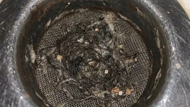 Close view of a drain strainer basket packed with hair and grease