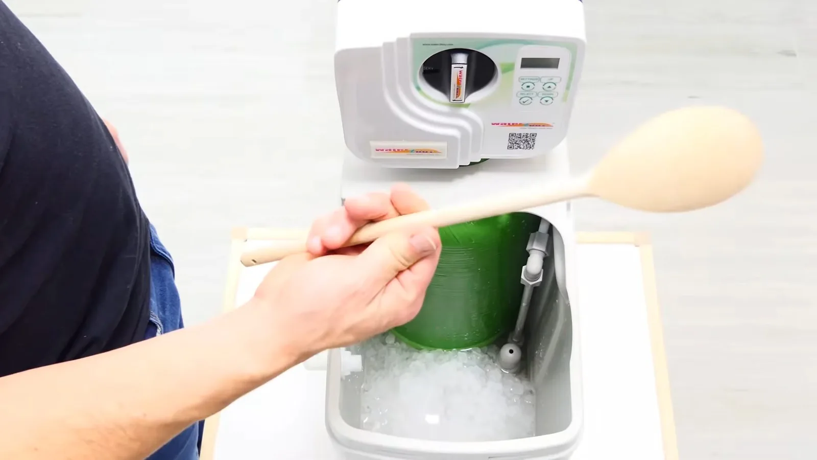 Hand using a wooden spoon to add salt to a white water softener