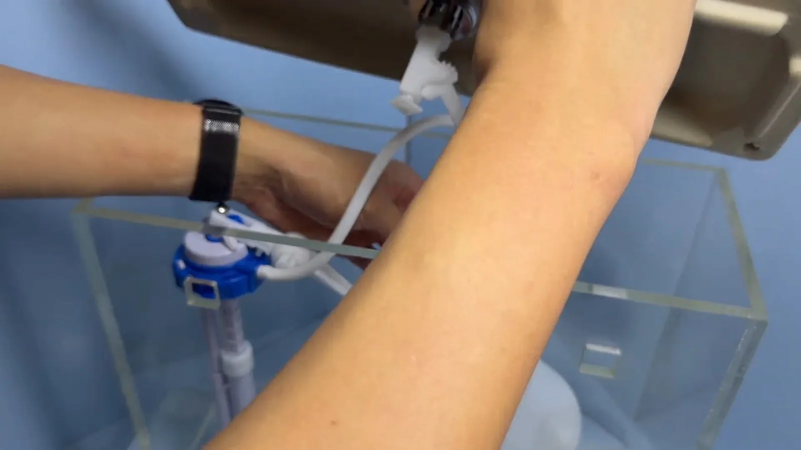 Hand adjusting a blue fill valve with a float inside a clear acrylic toilet tank
