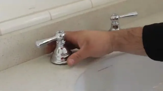 Hand at the base of a chrome bathroom faucet on a sink