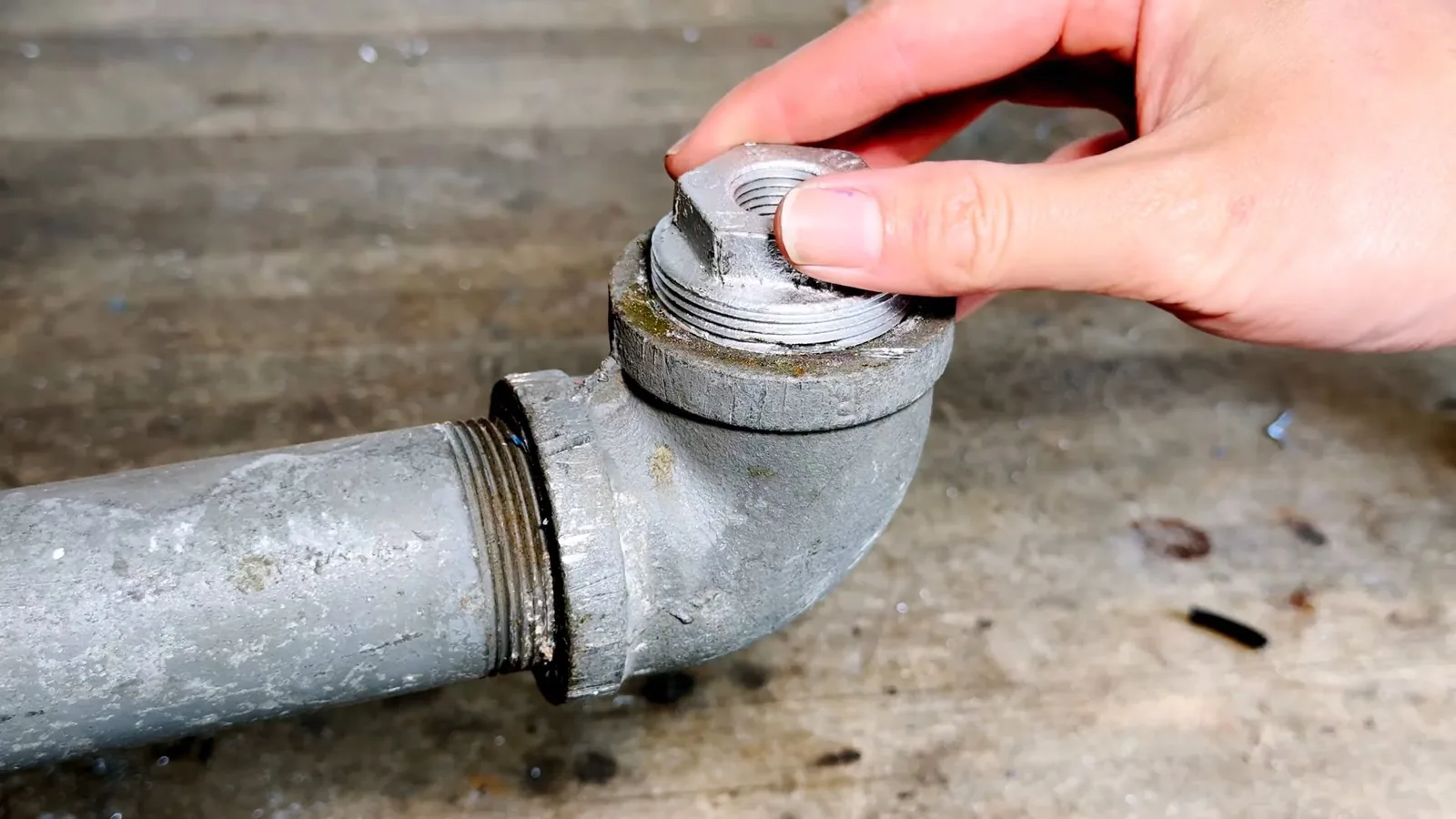Hand resting on a galvanized steel elbow with a threaded joint
