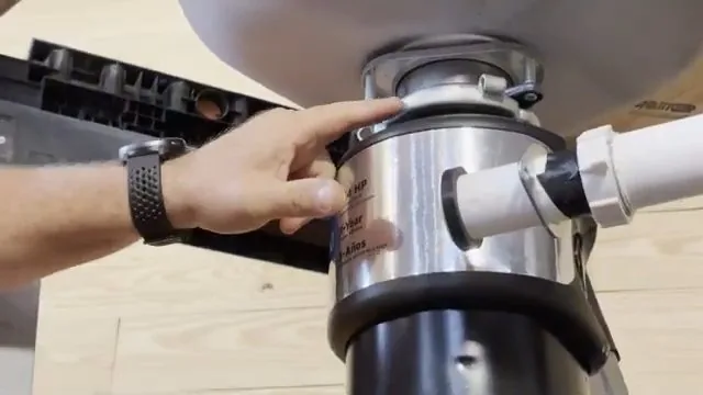 Hand resting on the casing of a garbage disposal mounted under a sink with the discharge pipe attached