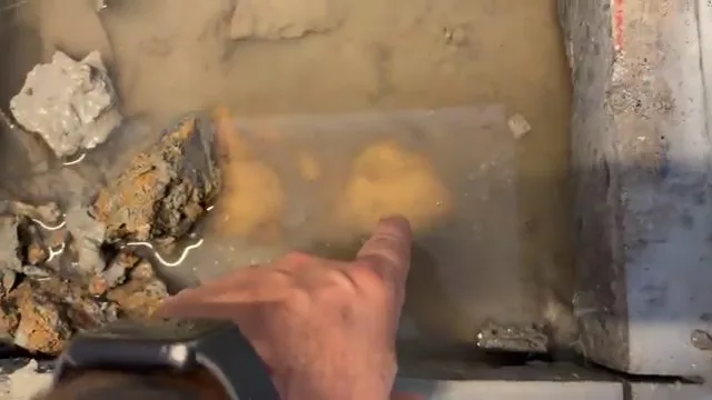 Hand pointing at standing water in an opened section of a concrete slab floor
