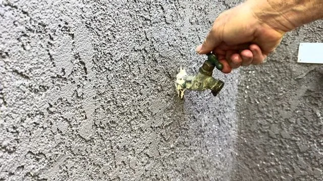 Hand turning the handle of an outdoor hose bib on a stucco wall