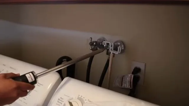 Hand with a tool at the supply valves behind a washing machine
