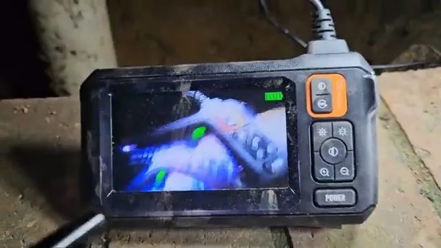 Handheld inspection monitor showing the inside of a pipe with a camera cable running out of it