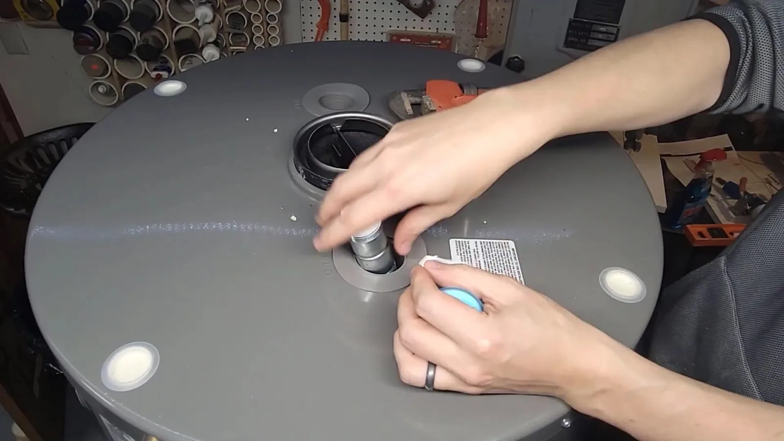 Hands working at a fitting on top of a grey tank water heater