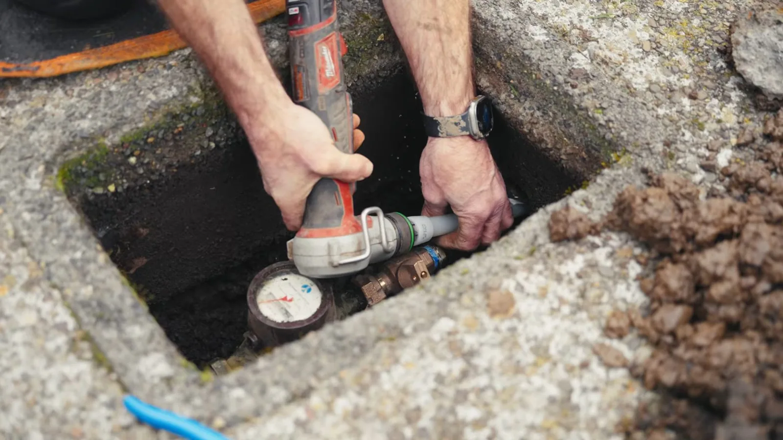 Hands holding a tool inside a concrete water meter box