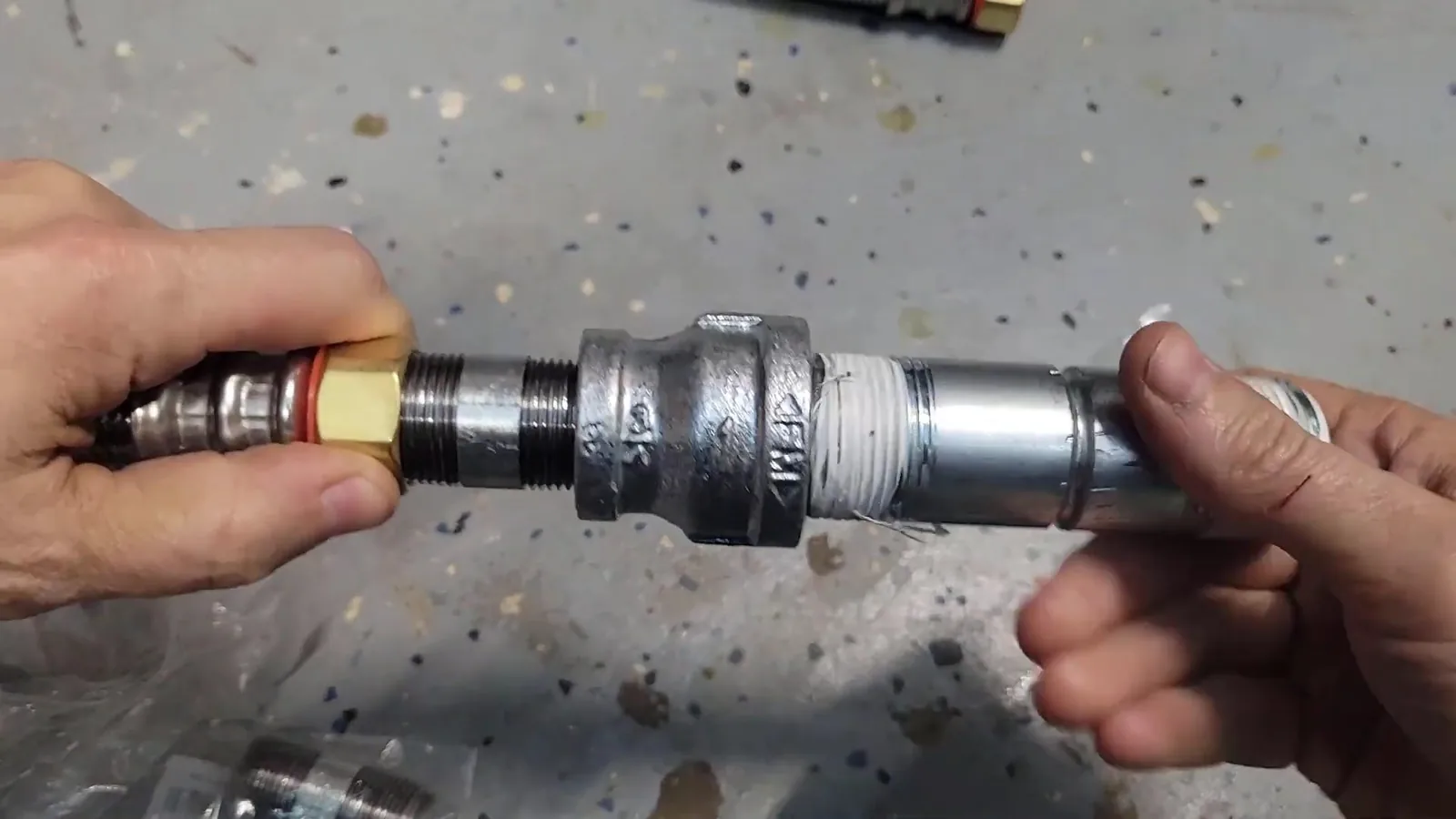 Hands holding a galvanized steel nipple with white thread tape next to a fitting