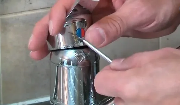 Hands removing the cap screw from a chrome faucet handle with a hex key