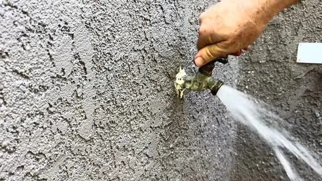 Outdoor hose bib on a stucco wall with water spraying out