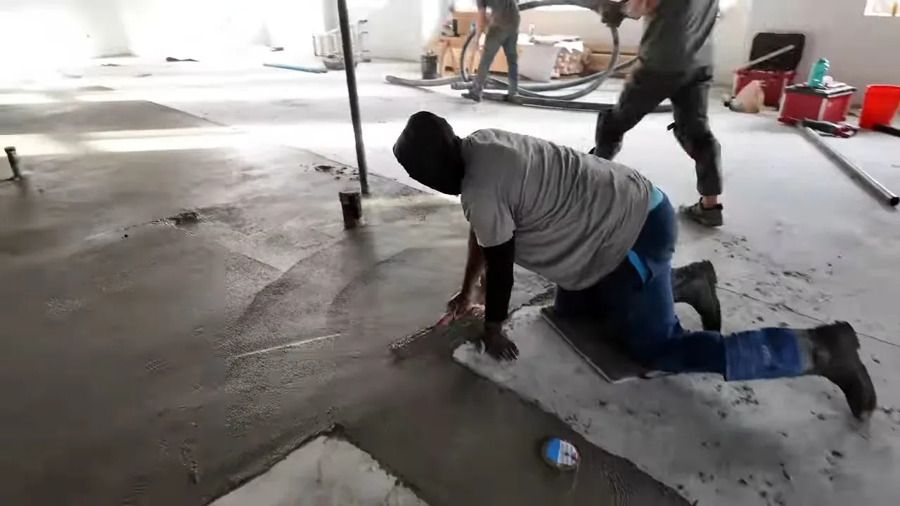 Man kneeling on a fresh concrete slab patch while another stands behind him