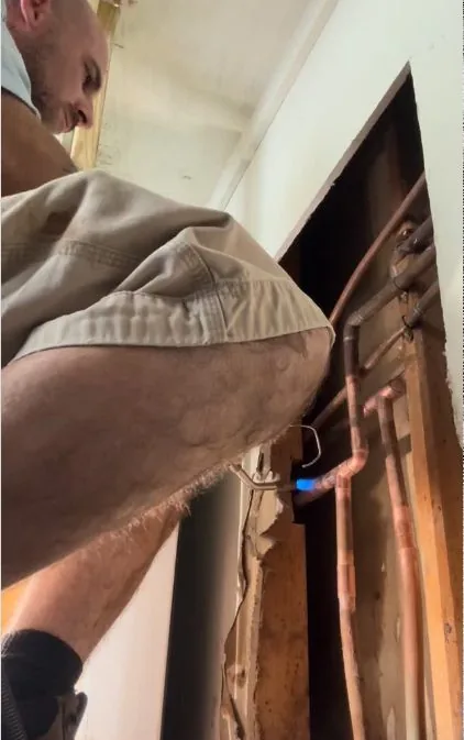 Man looking into an opened section of wall with copper pipes inside