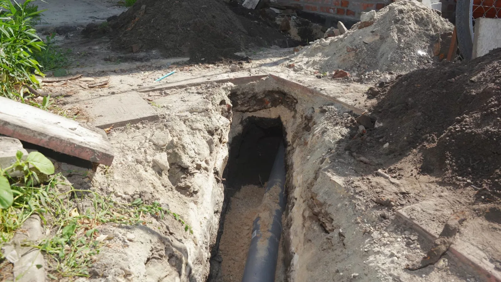 Open trench beside a house with a black sewer pipe lying in it