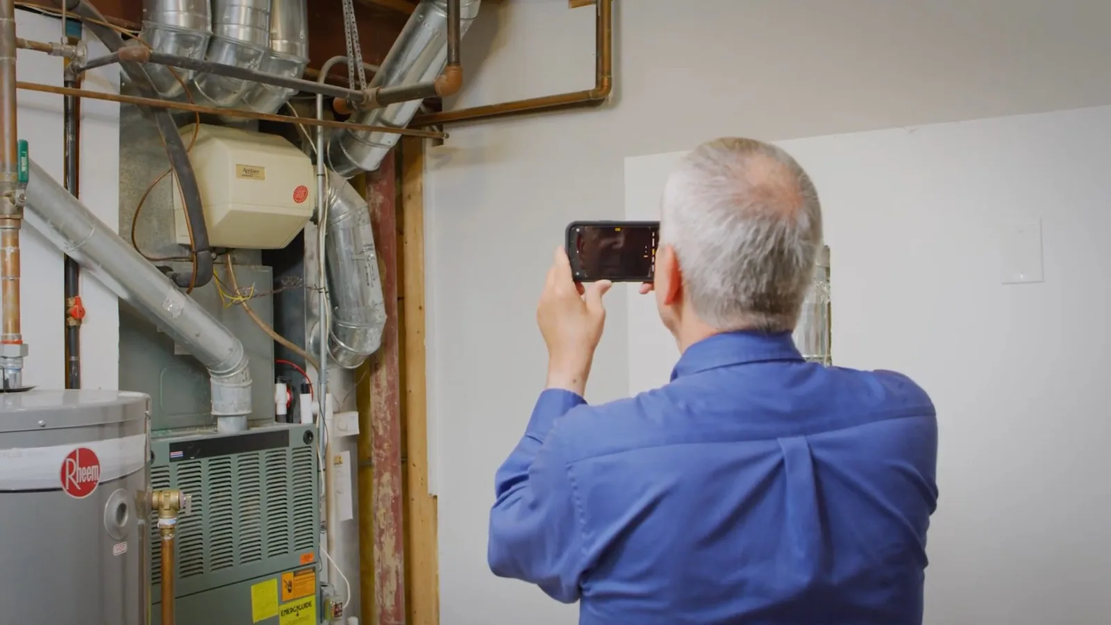 Man crouching at a water heater closet taking a photo with a phone