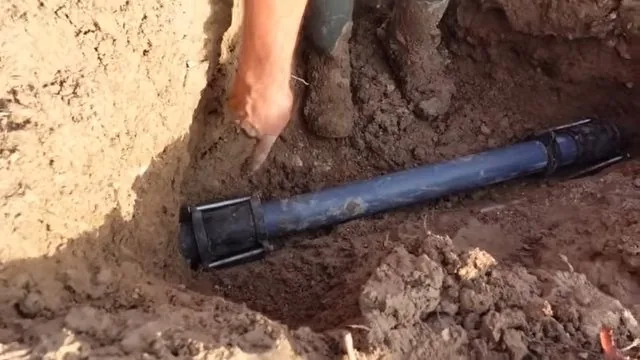 Man pointing at a dark pipe lying in a muddy trench