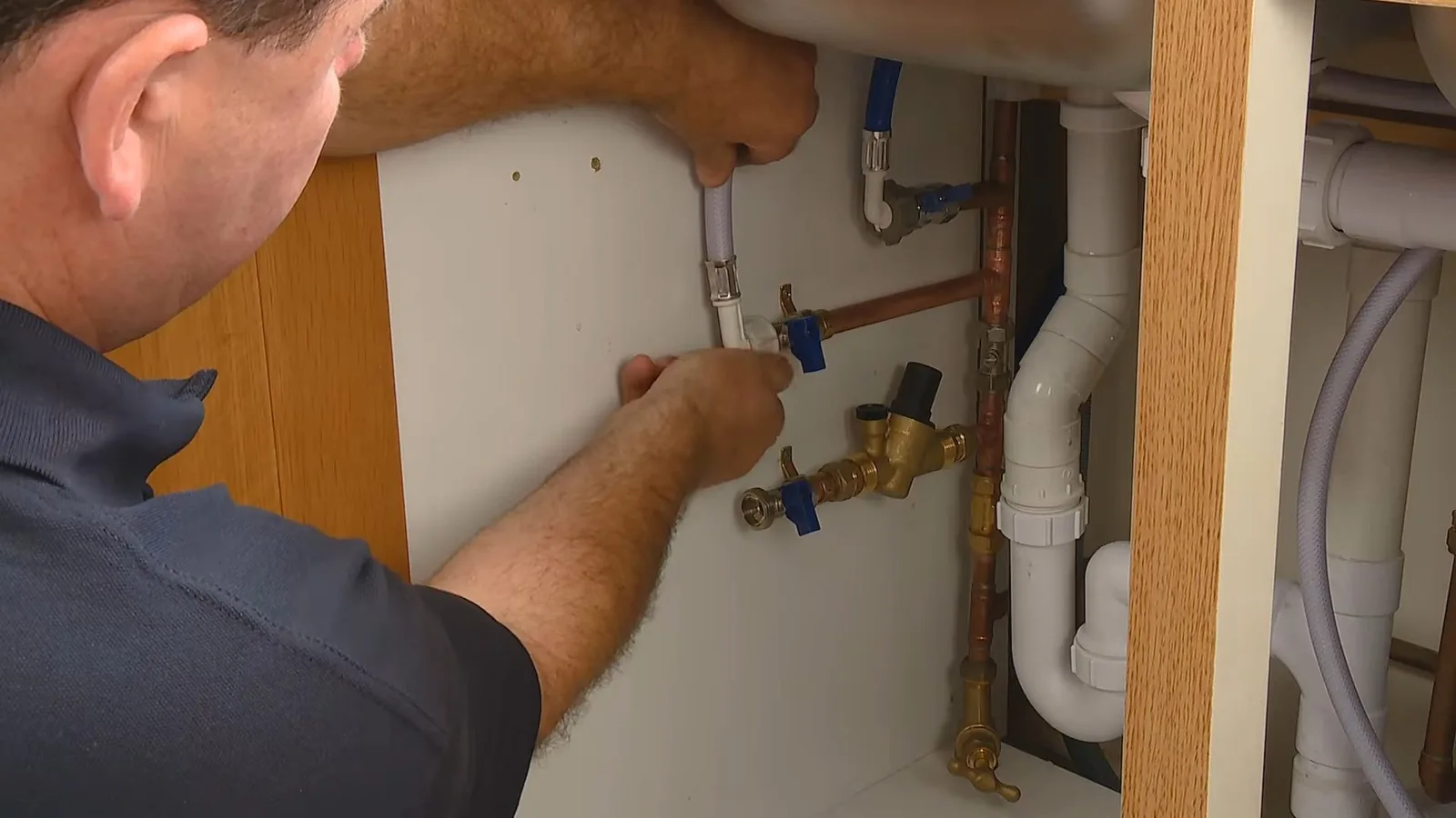 Man reaching up to the supply valves under a sink beside the drain trap