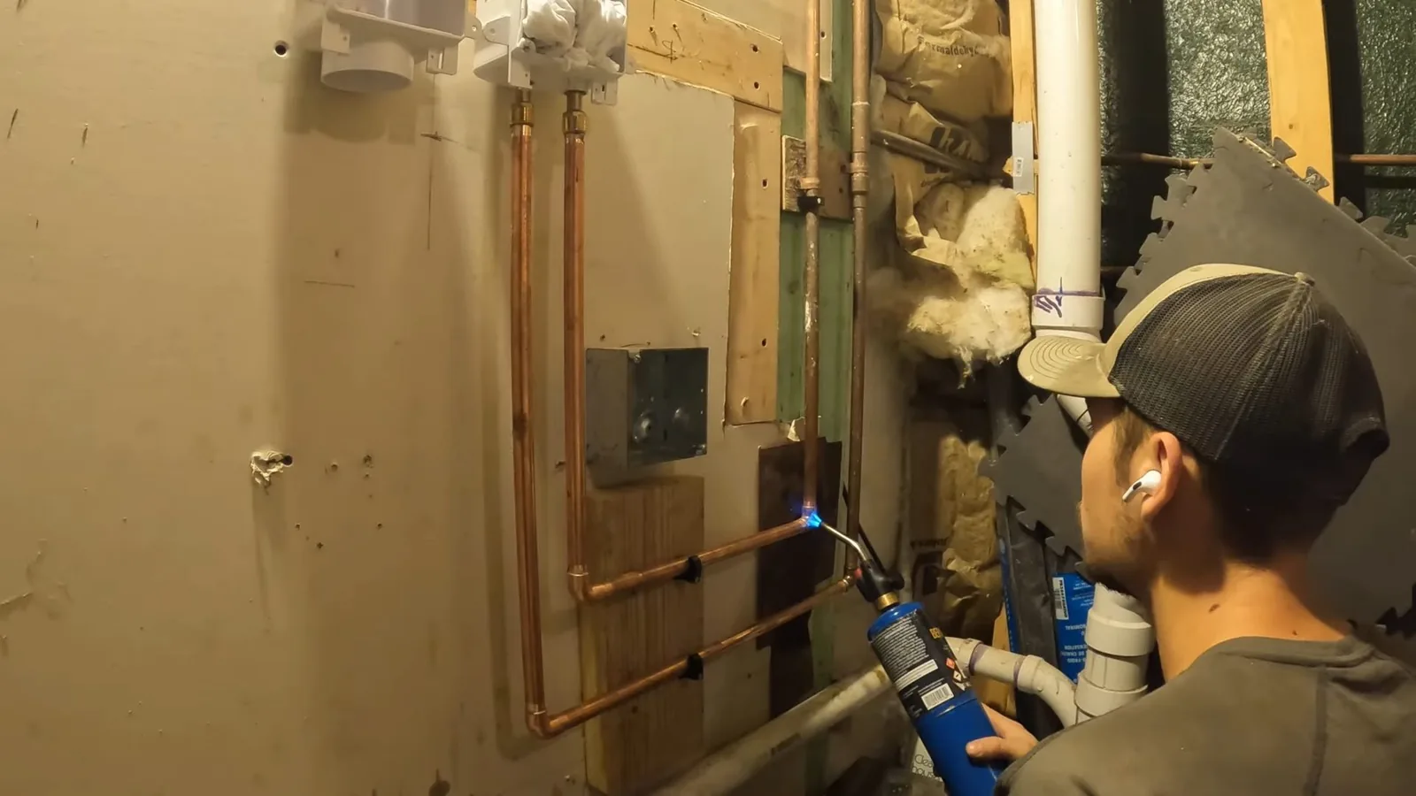 Man in a cap using a torch on copper pipe on a basement wall