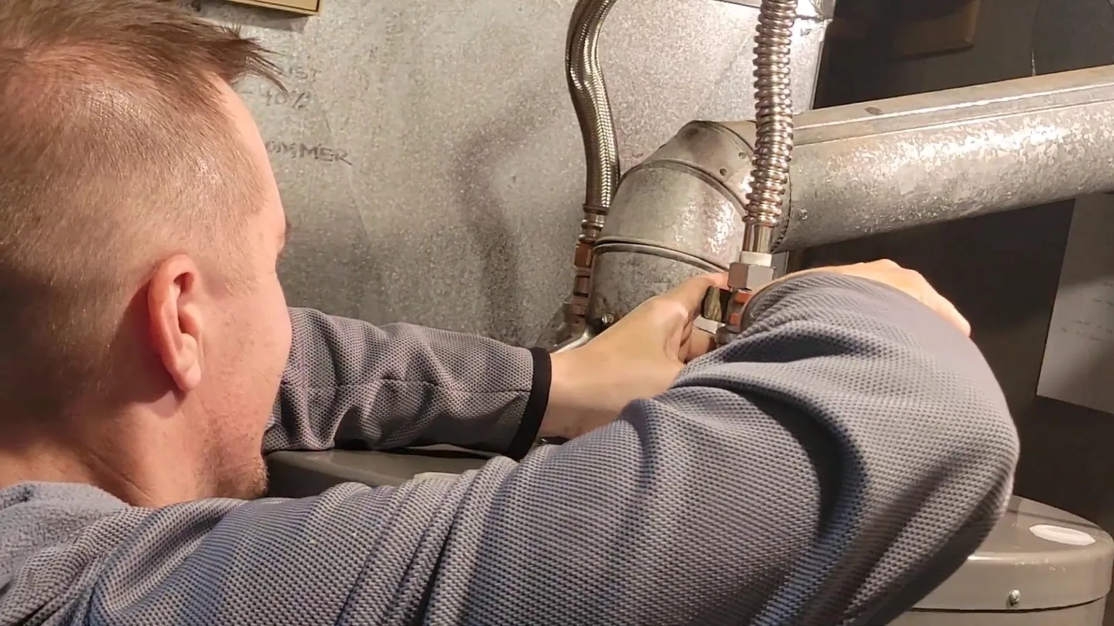 Man leaning in to work at the top connections of a tank water heater beside a flexible gas line