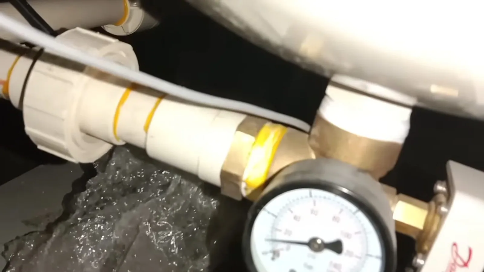 Round pressure gauge screwed into a fitting on a white water line with a brass valve